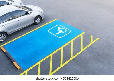 International handicapped symbol painted in bright blue on a shopping center parking space. The space is clearly marked on either side with additional white diagonal stripes.