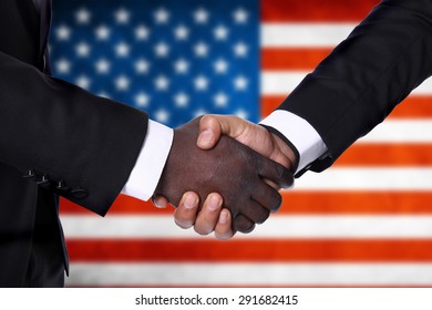 International Handshake with white and dark skinned businessman on background of the USA flag. - Powered by Shutterstock