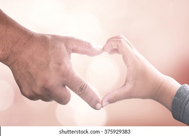 International human solidarity day concept: Father and son hands make heart shape over blurred pink nature background