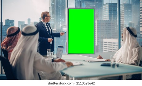 International Manager Holds Meeting Presentation For Saudi Business Partners. Specialist Uses Whiteboard With Vertical Green Screen Mock Up Display. Saudi, Emirati, Arab Office Concept.