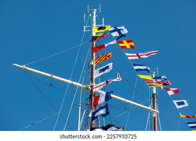 International maritime signal flags on a flagpole and masts on a sailing ship with a blue sky in the background - Shutterstock ID 2257933725