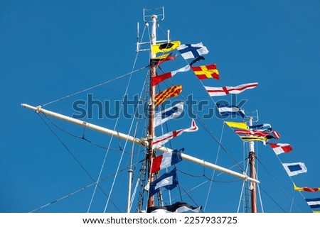 International maritime signal flags on a flagpole and masts on a sailing ship with a blue sky in the background
