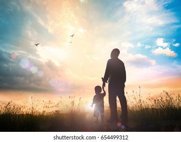 International migrants day concept: Silhouettes father and son holding hand in hand on meadow autumn sunset background - Shutterstock ID 654499312