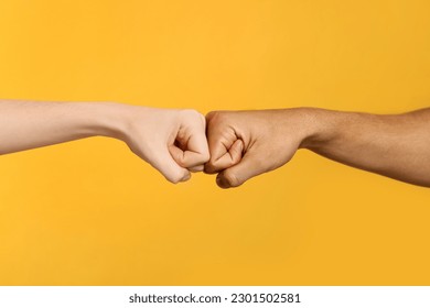 International relationships. People making fist bump on orange background, closeup