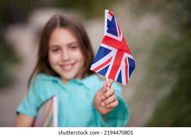 International School Student, Schoolgirl With UK Flag. Smiling Girl Handed You The Flag. Selective Focus. Concept Of Learning English, Summer Language School, Development. Caucasian 10 Years Old Child