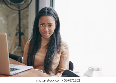 International Student Girl Is Studying Online By Using A Portable Computer Connected The Wifi Network. Web Designer Is Working On A New Project By A Laptop While Sitting In A Modern Coffee Shop.