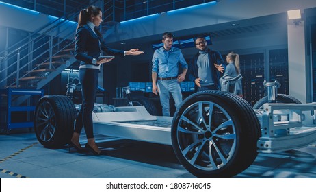 International Team Of Automobile Design Engineers Talking And Designing Autonomous Electric Car. Vehicle Platform Chassis Has Wheels, Engines, Battery. Evolution Of Clean Renewable Energy Efficiency