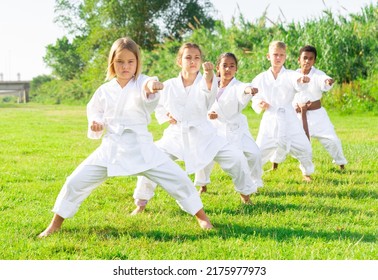 International Team Of Tweens In White Kimonos Exercising New Techniques During Outdoors Group Taekwondo Class On Green Lawn On Summer Day