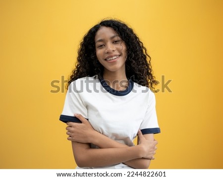 International Woman day power African American woman huge  embraces equity herself, feels good, fulfilled, has high self esteem, tilts head and smiling wears white shirt isolated on yellow background.