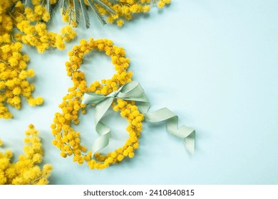 International Women's Day. A banner, a flyer, a beautiful postcard for March 8th. Yellow mimosa flowers in the shape of the number eight and a ribbon bow on a turquoise, blue background.