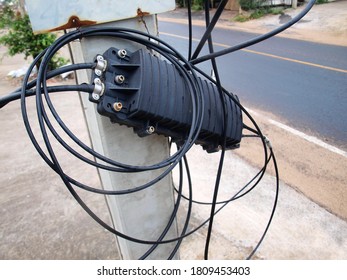 The Internet Box Is Damaged. A Black Plastic Box For Cable Connections, Hanging On The Pole Side With Messy Cables. On The Background Of The Paved Road. Focus Close And Choose The Subject.