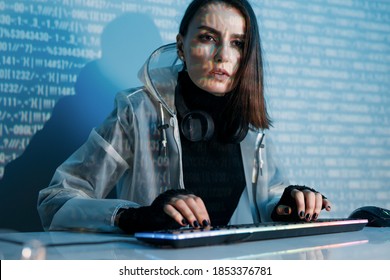 Internet, crime, cyber attack, system breaking concept. Blue neon light background. Woman hacker using computer with a binary code digital interface.