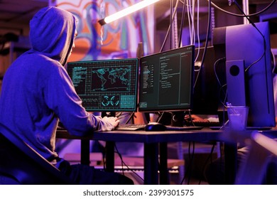 Internet criminal hacking computer network system and running ransomware code on screen. Man in hood breaking law while getting illegal access into database server in dark warehouse