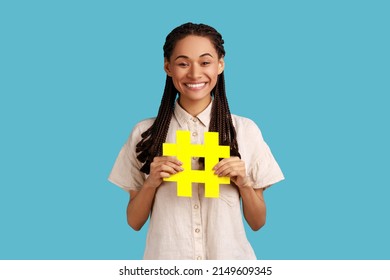 Internet Popularity. Portrait Of Happy Woman With Black Dreadlocks Holding Hashtag Symbol, Promoting Viral Topic In Social Network, Tagging Blog Trends. Indoor Studio Shot Isolated On Blue Background.