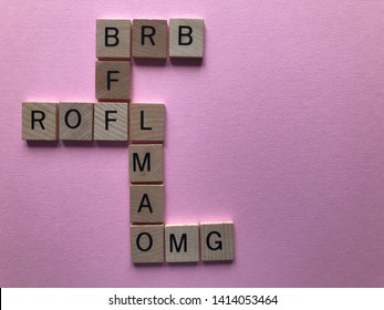 Internet slang. Acronyms : BRB (Be Right Back), BFF, ROFL, OMG, and LMAO used as abbreviations in text messages, in wooden letters in crossword form, on a pink background with copy space.