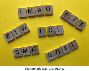 Internet slang. Acronyms : BTW (By The Way), ROFL, LOL, FYA, SMH, and LMAO used as abbreviations in text messages, in wooden alphabet letters on a bright yellow background 
