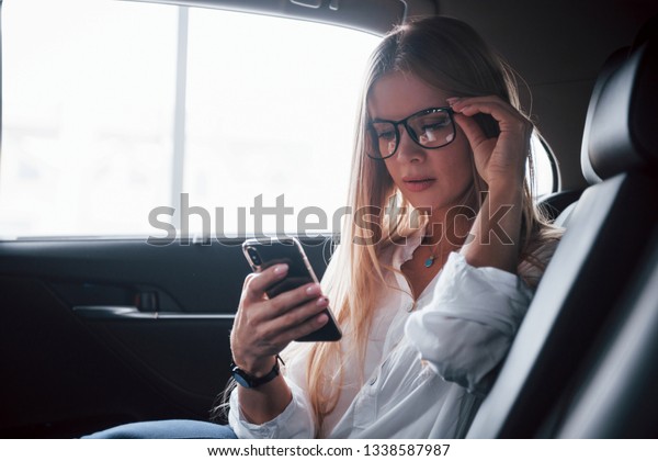 Internet surfing. Smart\
businesswoman sits at backseat of the luxury car with black\
interior.