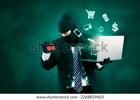 Internet Theft - hacker wearing a mask and holding a laptop and credit card