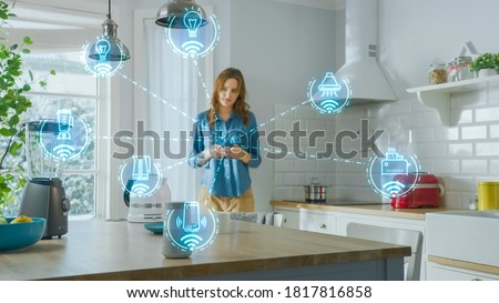 Internet of Things Concept: Young Woman Using Smartphone in Kitchen. She controls her Kitchen Appliances with IOT. Graphics Showing Digitalization Visualization of Connected Home Electronics Devices