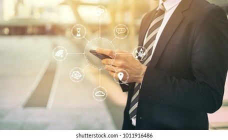 Internet Of Things(IOT) Concept With Young Man Holding His Smartphone  By Hand With Mobile Network Communication Technology, Diagram Showing Many Connected Devices Icons.