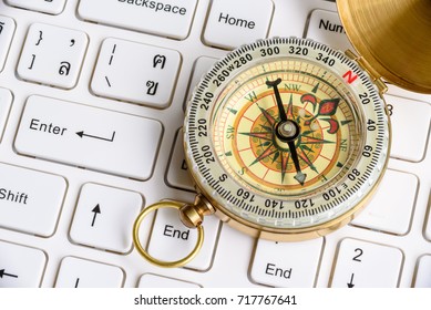 Internet www and website navigation concept : Vintage or retro style compass with brass cover put near an enter button or return key on a white desktop computer keyboard.