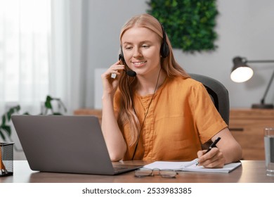 Interpreter in headphones taking notes while working with laptop at table indoors