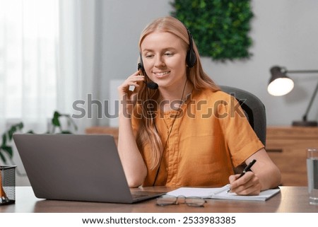 Interpreter in headphones taking notes while working with laptop at table indoors