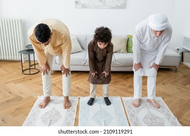 Interracial barefoot men and muslim kid standing on rugs at home