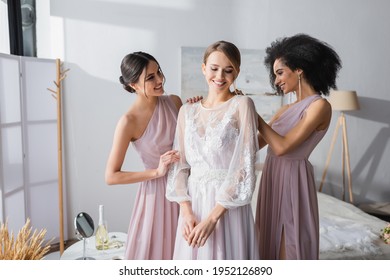 interracial bridesmaids dressing happy bride in bedroom - Powered by Shutterstock