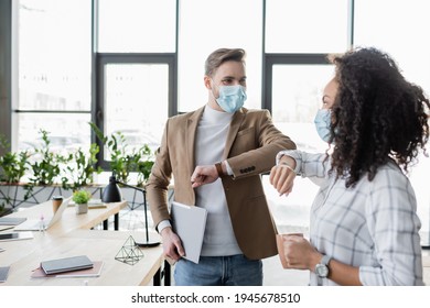 Interracial Business Partners In Medical Masks Doing Elbow Greeting In Office