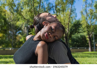 Interracial Couple, Black African Woman, Leaning On The Shoulder Of Her Partner A Long Haired Latin American Man. The Woman Looks Straight Into The Camera.