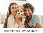 Interracial couple cuddles their corgi at home, smiling and cherishing time together, showcasing love and togetherness with their furry companion. Relationship concept
