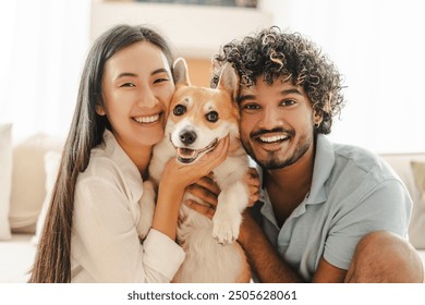 Interracial couple cuddles their corgi at home, smiling and cherishing time together, showcasing love and togetherness with their furry companion. Relationship concept - Powered by Shutterstock