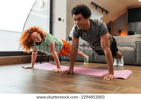 An interracial couple doing push ups together in the living room, is dressed casually and they like to exercise together