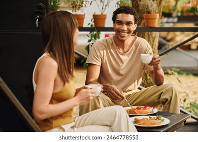 An interracial couple enjoying a meal together on a bench, savoring their food in a cozy and intimate setting. - Powered by Shutterstock