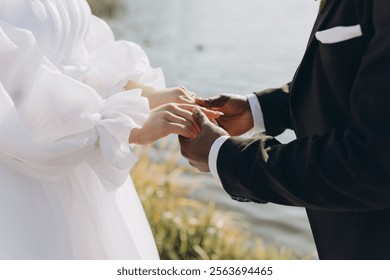 Interracial couple exchanging rings during wedding ceremony by the lake, symbolizing their union and commitment - Powered by Shutterstock