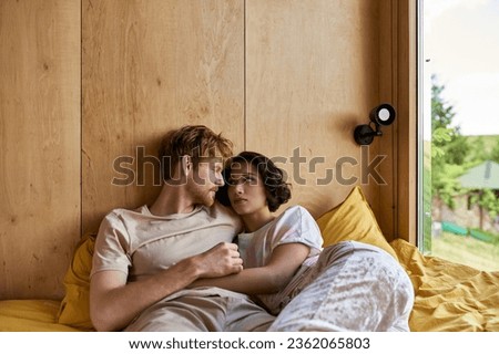interracial couple having tender moment while lying together on bed and looking at each other