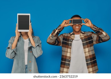 interracial couple holding smartphone and digital tablet with blank screen on blue backdrop - Shutterstock ID 2363752219