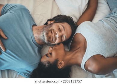 Interracial couple, kiss and relax on bed above for morning bonding, intimate relationship or love at home. Top view of woman kissing man while lying in bedroom for loving romance, care or affection - Powered by Shutterstock