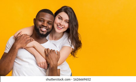 Interracial couple in love. Portrait of happy multiracial sweethearts embracing and posing together over yellow background, panorama with copy space