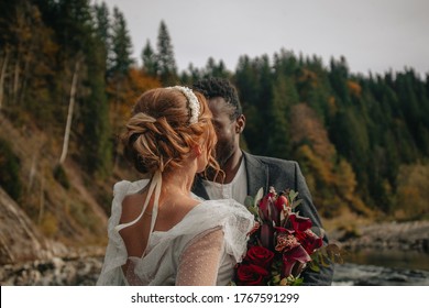 an interracial couple of newlyweds walks along the shore of a mountain river. Mountain wedding. Mountains of Ukraine - Shutterstock ID 1767591299