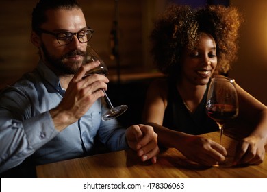 Interracial couple on date: handsome Caucasian man in shirt and glasses holding glass of red wine, sitting at table with his beautiful African girlfriend, enjoying nice evening together at restaurant - Powered by Shutterstock