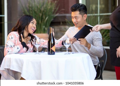 Interracial Couple On A Date Paying For A Restaurant Tab With A Waitress. They Are In An Outdoor Cafe Handling The Payment Bill And Server Tip Or Gratuity.