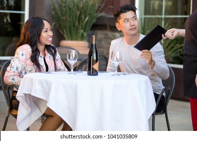 Interracial Couple On A Date Paying For A Restaurant Tab With A Waitress. They Are In An Outdoor Cafe Handling The Payment Bill And Server Tip Or Gratuity.