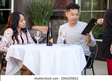 Interracial Couple On A Date Paying For A Restaurant Tab With A Waitress. They Are In An Outdoor Cafe Handling The Payment Bill And Server Tip Or Gratuity.