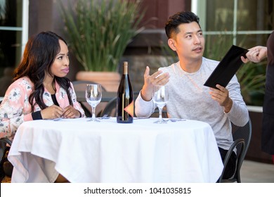 Interracial Couple On A Date Paying For A Restaurant Tab With A Waitress. They Are In An Outdoor Cafe Handling The Payment Bill And Server Tip Or Gratuity.