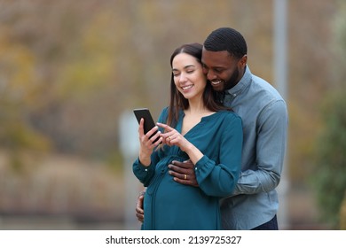 Interracial couple with a pregnant wife and her husband checking smart phone in a park