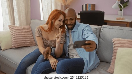 Interracial couple sitting on a sofa in a cozy living room, taking a selfie together, showcasing their love and happiness at home. - Powered by Shutterstock