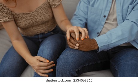 Interracial couple sitting together at home holding hands in a living room displaying affection and unity - Powered by Shutterstock