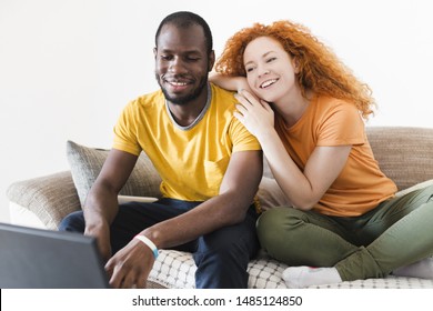 Interracial couple smiling at a laptop in a photo studio with white background